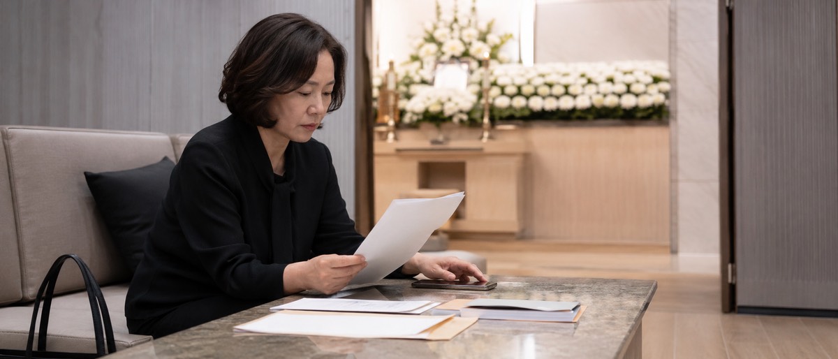 장례식장 가족 대기실에서 서류와 휴대폰을 확인하는 여성 유족
